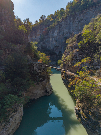 Aerial view of Osumi Canyon featuring a narrow gorge with a turquoise river a wooden footbridge and steep rocky cliffs with lush vegetation in Dhores Berat County Albania.