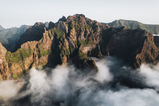 Aerial view of rugged peaks pierce through a sea of ethereal clouds sunlight casting shadows on the dramatic landscape Pico do Areeiro Madeira Portugal.