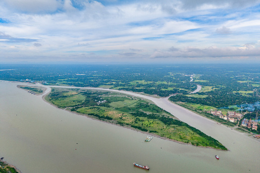 Aerial view of Char Bakalia surrounded by the river lush green fields and industrial structures under a blue sky in Chittagong District Chittagong Division Bangladesh.