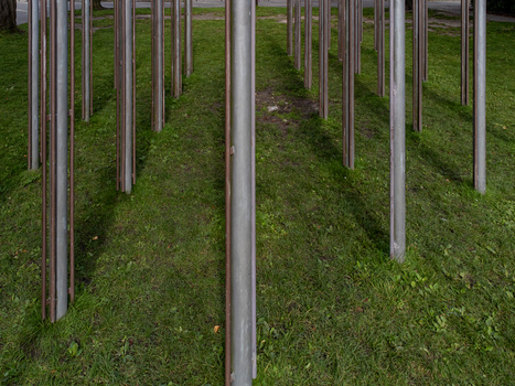 Aerial view of metallic pillars piercing through a carpet of vivid green grass creating a stark contrast between industrial and natural elements Almere Flevoland Netherlands.