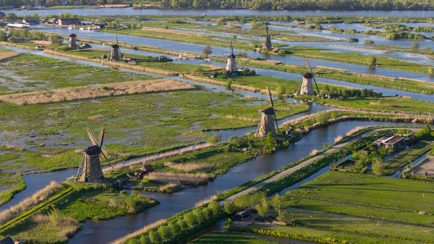 Aerial view of the historic Kinderdijk windmills standing along narrow canals and lush green polder fields under soft afternoon light in Kinderdijk South Holland Netherlands. Aerial view of the historic Kinderdijk windmills standing along narrow canals and lush green polder fields under soft afternoon light in Kinderdijk South Holland Netherlands.