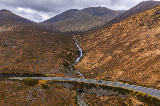 Aerial view of Eas a Bhradain waterfall cascading through a rugged mountain valley towards a winding road Isle of Skye Scotland United Kingdom. Aerial view of Eas a Bhradain waterfall cascading through a rugged mountain valley towards a winding road Isle of Skye Scotland United Kingdom.