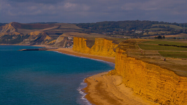 Aerial view of the dramatic golden sandstone cliffs of West Bay meeting the turquoise waters of the English Channel under a cloudy sky in West Bay England United Kingdom. Aerial view of the dramatic golden sandstone cliffs of West Bay meeting the turquoise waters of the English Channel under a cloudy sky in West Bay England United Kingdom.