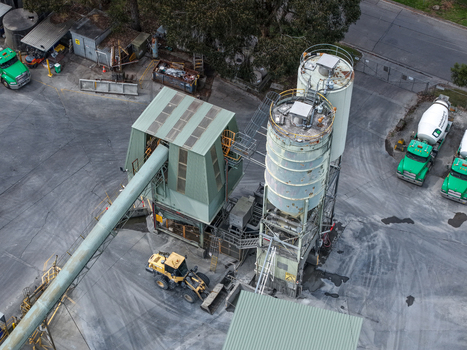 Melbourne VIC Australia 25 September 2026 Aerial view of an industrial concrete plant with tall storage silos a long conveyor belt a yellow front end loader and green trucks in a yard.