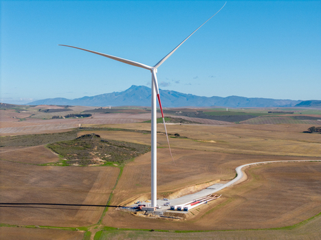 Aerial view of a large wind turbine standing in a vast rural landscape with rolling hills and distant mountains under a clear blue sky Swellendam Western Cape South Africa. Aerial view of a large wind turbine standing in a vast rural landscape with rolling hills and distant mountains under a clear blue sky Swellendam Western Cape South Africa.