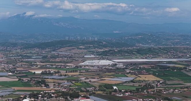 Aerial view of the valley with greenhouses and wind turbines Italy.