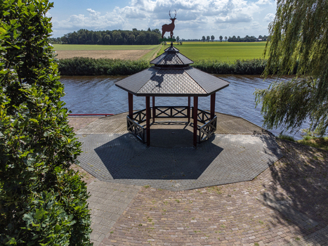 Aerial view of a gazebo topped with a deer statue standing proudly against a backdrop of green fields and a tranquil canal Tollebeek Flevoland Netherlands.
