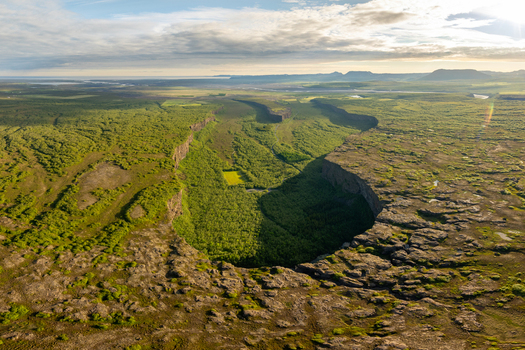 Aerial view of the horseshoe shaped Asbyrgi canyon featuring lush green forests dramatic steep cliffs and surrounding volcanic terrain in Nordurthing Iceland.