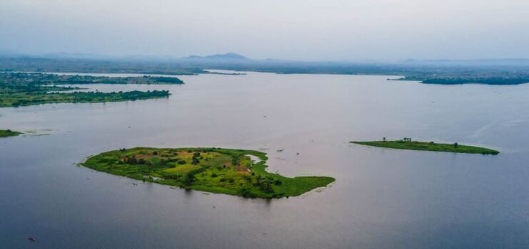 Aerial view of small islands with lush green vegetation surrounded by the calm waters of a vast lake under a hazy sky in Ghana. Aerial view of small islands with lush green vegetation surrounded by the calm waters of a vast lake under a hazy sky in Ghana.
