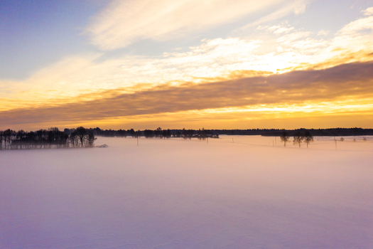Aerial view of a vast snow covered field blanketed in thick morning mist under a vibrant golden sunrise in Latvia. Aerial view of a vast snow covered field blanketed in thick morning mist under a vibrant golden sunrise in Latvia.