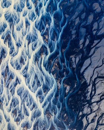 Aerial view of the intricate braided river channels with dark glacial sediment and blue water flowing across the volcanic landscape of Iceland. Aerial view of the intricate braided river channels with dark glacial sediment and blue water flowing across the volcanic landscape of Iceland.