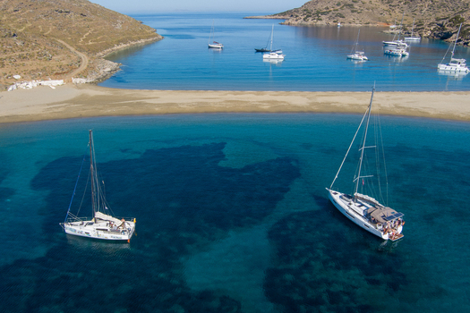 Greece 21 September 2026 Aerial view of sailboats anchored in the turquoise waters of a double sided beach in Greece with rocky hills and clear blue sky. Greece 21 September 2026 Aerial view of sailboats anchored in the turquoise waters of a double sided beach in Greece with rocky hills and clear blue sky.