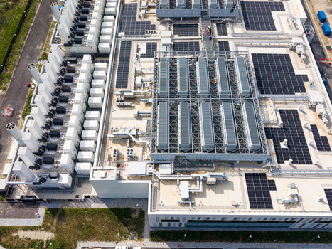 Aerial view of a modern data center campus featuring extensive rooftop solar panels and industrial cooling infrastructure in Melegnano Lombardy Italy.