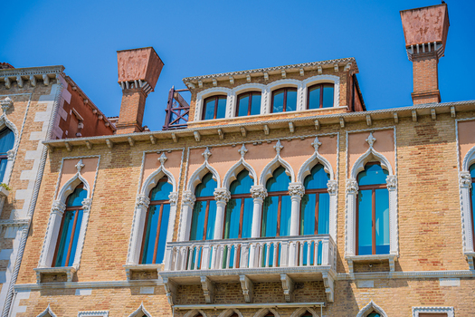 Venice Italy 29 March 2026 View of an ornate building facade with arched windows reflecting the azure sky framed by salmon and brick hues. Venice Italy 29 March 2026 View of an ornate building facade with arched windows reflecting the azure sky framed by salmon and brick hues.