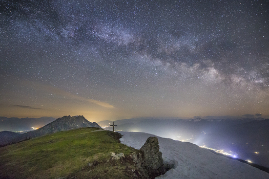 View of the Stoderzinken summit cross under the Milky Way galaxy and a starry night sky with valley lights Liezen Steiermark Austria. View of the Stoderzinken summit cross under the Milky Way galaxy and a starry night sky with valley lights Liezen Steiermark Austria.