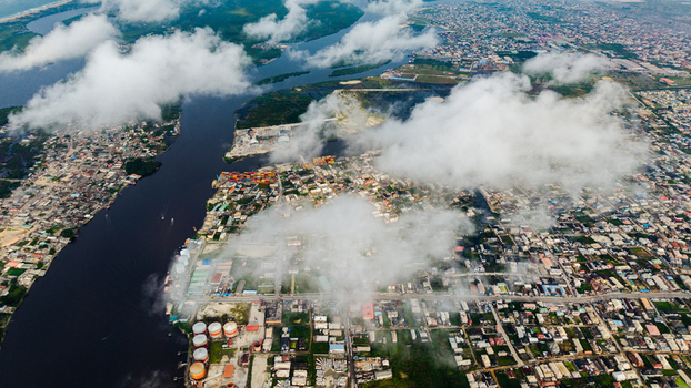 Aerial view of Satellite Town featuring industrial storage tanks dense urban housing and a winding river under a cloudy sky in Lagos Lagos Nigeria.