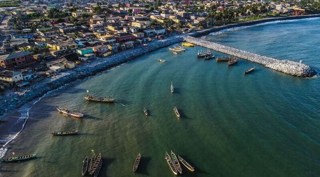 Aerial view of traditional wooden fishing boats anchored in a coastal bay near a stone breakwater and a densely populated town in Ghana. Aerial view of traditional wooden fishing boats anchored in a coastal bay near a stone breakwater and a densely populated town in Ghana.