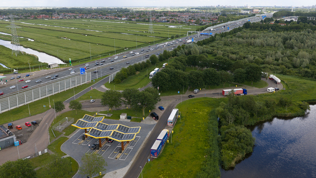Oostzaan Netherlands 09 June 2026 Aerial view of Fastned charging station with solar panel roofs near a busy highway surrounded by green fields and water in the Dutch countryside.