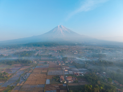 Aerial view of Mount Semeru rising above the misty agricultural fields and village of Sumberurip in Pronojiwo East Java Indonesia. Aerial view of Mount Semeru rising above the misty agricultural fields and village of Sumberurip in Pronojiwo East Java Indonesia.