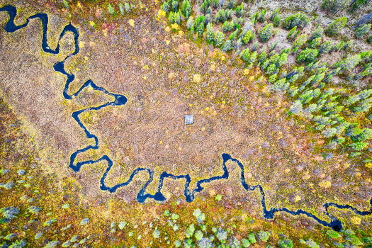Aerial view of a winding river flowing through a colorful autumn marshland surrounded by dense evergreen and deciduous forests in Enontekio Lapland Finland. Aerial view of a winding river flowing through a colorful autumn marshland surrounded by dense evergreen and deciduous forests in Enontekio Lapland Finland.