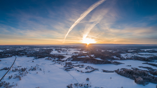 Aerial view of a snowy landscape in Latvia at sunrise featuring frozen fields dense forests and a winding road under a clear sky with contrails Latvia. Aerial view of a snowy landscape in Latvia at sunrise featuring frozen fields dense forests and a winding road under a clear sky with contrails Latvia.