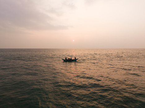 Aerial view of a small fishing boat with fishermen on calm ocean waters under a hazy sunset sky in Galle Southern Province Sri Lanka.