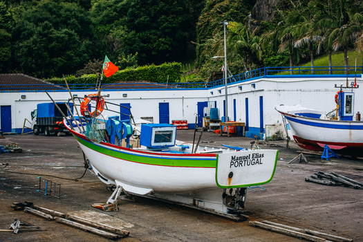 View of a vibrant fishing boat with the Portuguese flag proudly displayed sitting on a textured ground near white buildings São Miguel Portugal. View of a vibrant fishing boat with the Portuguese flag proudly displayed sitting on a textured ground near white buildings São Miguel Portugal.