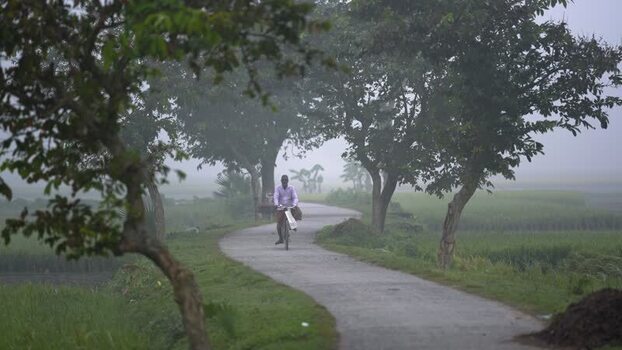 View of a man riding a bicycle on a rural road in the fog Bangladesh. View of a man riding a bicycle on a rural road in the fog Bangladesh.