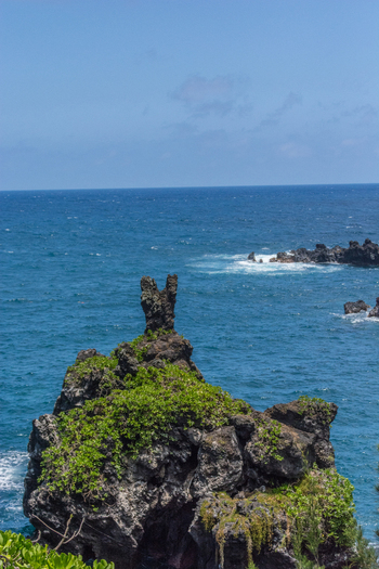 View of a volcanic sea stack covered in lush green vegetation rising from the deep blue Pacific Ocean in Maui County Hawaii United States.