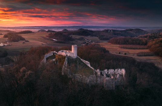 Aerial view of the medieval castle ruins in the Krakow Czestochowa Upland surrounded by dense forest under a dramatic sunset sky Krakow County Lesser Poland Voivodeship Poland. Aerial view of the medieval castle ruins in the Krakow Czestochowa Upland surrounded by dense forest under a dramatic sunset sky Krakow County Lesser Poland Voivodeship Poland.