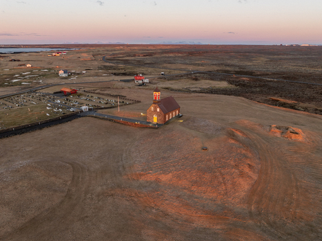 Aerial view of Hvalsneskirkja church surrounded by a historic cemetery and vast barren landscape under the warm light of the golden hour in Sudurnesjabaer Iceland. Aerial view of Hvalsneskirkja church surrounded by a historic cemetery and vast barren landscape under the warm light of the golden hour in Sudurnesjabaer Iceland.