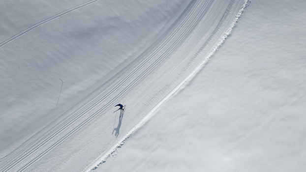 Aerial view of a solitary skier glides across the pristine snow covered expanse leaving delicate tracks in the shimmering landscape Mijoux Auvergne Rhône Alpes France. Aerial view of a solitary skier glides across the pristine snow covered expanse leaving delicate tracks in the shimmering landscape Mijoux Auvergne Rhône Alpes France.
