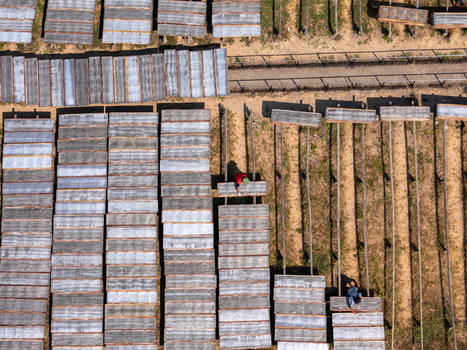 Aerial view of workers tending to rows of rectangular drying racks on dry soil in Polanharjo Central Java Indonesia.