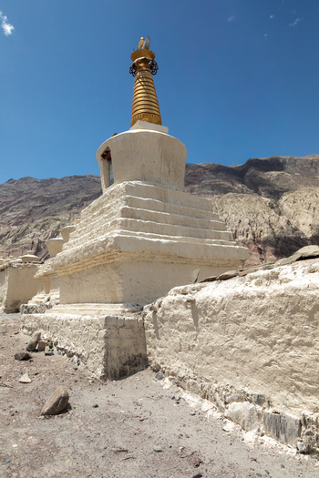 View of the white stupa at Charasa Gonpa with a golden spire set against arid mountains and a clear blue sky in Charasa Ladakh India.