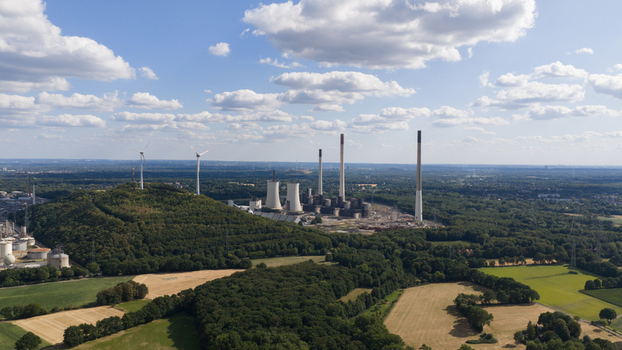 Aerial view of Scholven Power Station with tall chimneys and cooling towers surrounded by forests wind turbines and agricultural fields in Gelsenkirchen Nordrhein Westfalen Germany.