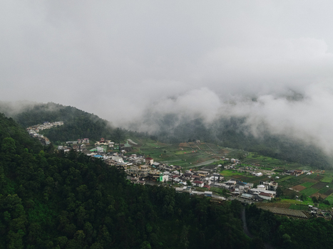 Aerial view of a mountain village nestled among lush green forests and agricultural fields under thick rolling mist in Tawangmangu Central Java Indonesia.