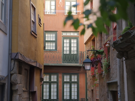 View of a narrow historic street featuring colorful traditional buildings with green window frames balconies and a hanging lantern in Porto Porto District Portugal. View of a narrow historic street featuring colorful traditional buildings with green window frames balconies and a hanging lantern in Porto Porto District Portugal.
