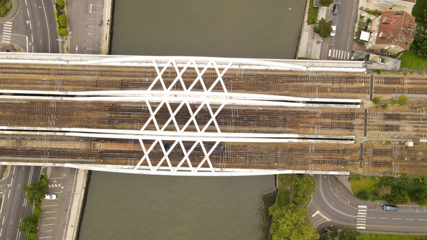 Aerial view of a white steel railway bridge crossing a river with train tracks and a train surrounded by urban roads and greenery in Pontoise Ile de France France. Aerial view of a white steel railway bridge crossing a river with train tracks and a train surrounded by urban roads and greenery in Pontoise Ile de France France.
