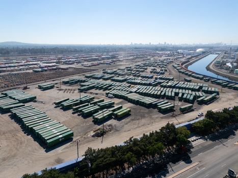 Aerial view of a vast industrial shipping container yard with rows of green containers a nearby canal and a road in Carson California United States.
