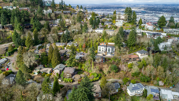 Aerial view of the Northwest Imperial Terrace neighborhood featuring residential homes nestled among lush green trees on a hillside with a city skyline in the distance in Portland Oregon United States. Aerial view of the Northwest Imperial Terrace neighborhood featuring residential homes nestled among lush green trees on a hillside with a city skyline in the distance in Portland Oregon United States.