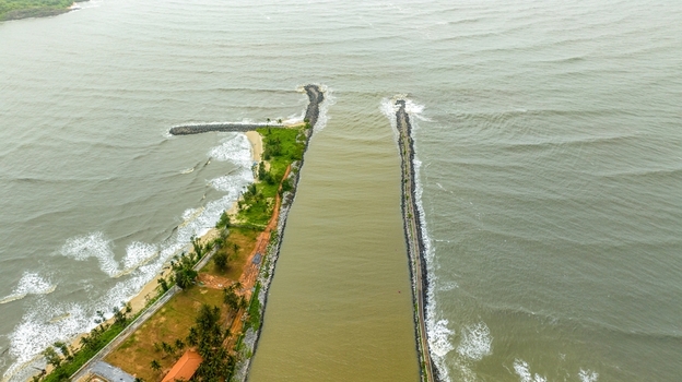 Aerial view of Malpe Fishing Harbour showing the channel entrance with stone breakwaters extending into the sea surrounded by coastal greenery and sandy shores in Udupi Karnataka India. Aerial view of Malpe Fishing Harbour showing the channel entrance with stone breakwaters extending into the sea surrounded by coastal greenery and sandy shores in Udupi Karnataka India.