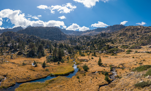 Aerial view of Llac de pessons surrounded by rocky mountains pine trees and a winding stream in the golden landscape of Grau Roig Encamp Andorra. Aerial view of Llac de pessons surrounded by rocky mountains pine trees and a winding stream in the golden landscape of Grau Roig Encamp Andorra.