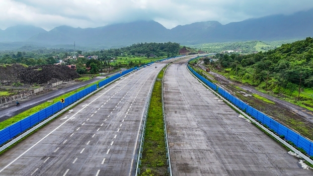 Aerial view of the Delhi Mumbai Expressway featuring multi lane concrete pavement blue safety barriers and lush green hills under a cloudy sky in Badlapur Maharashtra India. Aerial view of the Delhi Mumbai Expressway featuring multi lane concrete pavement blue safety barriers and lush green hills under a cloudy sky in Badlapur Maharashtra India.