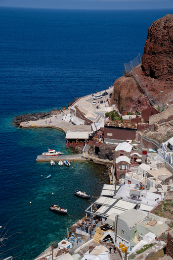 View of the Old Port of Fira with white buildings small boats moored in turquoise water and steep volcanic cliffs under a clear sky Fira Greece. View of the Old Port of Fira with white buildings small boats moored in turquoise water and steep volcanic cliffs under a clear sky Fira Greece.