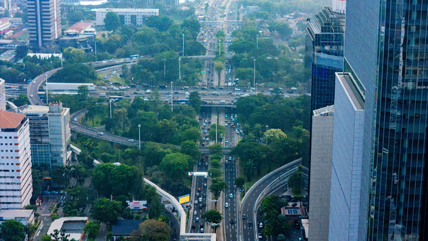 Aerial view of a busy highway interchange surrounded by modern skyscrapers lush green trees and dense urban infrastructure in Jakarta Indonesia.