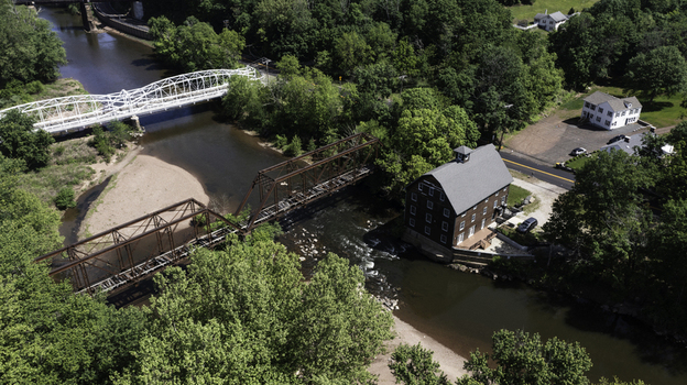 Aerial view of the historic Neshanic Station mill building situated beside the Neshanic River with its iconic truss bridge and surrounding lush greenery in Branchburg New Jersey United States.