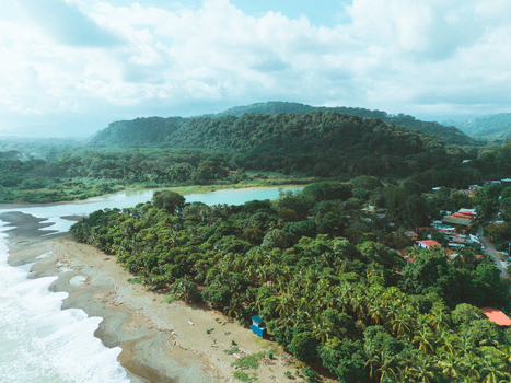 Aerial view of a tropical coastline featuring a sandy beach dense green forest a river mouth and a small coastal village with houses nestled among palm trees in Costa Rica.