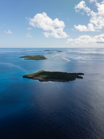 Aerial view of small islands scattered across the deep blue sea contrasting with the bright sky and scattered clouds Ouvéa Loyalty Islands Province New Caledonia. Aerial view of small islands scattered across the deep blue sea contrasting with the bright sky and scattered clouds Ouvéa Loyalty Islands Province New Caledonia.