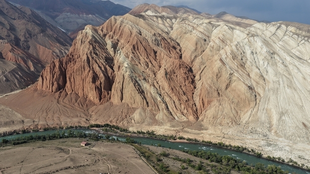 Aerial view of the dramatic multi colored layered mountains and a winding river flowing through the arid landscape of the Naryn Region Kyrgyzstan. Aerial view of the dramatic multi colored layered mountains and a winding river flowing through the arid landscape of the Naryn Region Kyrgyzstan.