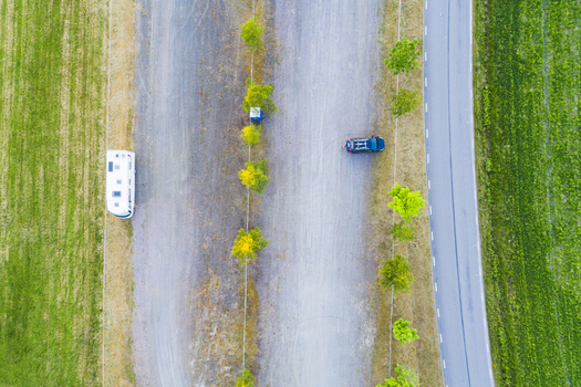 Aerial view of a camper van and a car parked on a gravel lot beside a road surrounded by lush green fields and a line of trees in Vanersnas Vastra Gotalands lan Sweden. Aerial view of a camper van and a car parked on a gravel lot beside a road surrounded by lush green fields and a line of trees in Vanersnas Vastra Gotalands lan Sweden.
